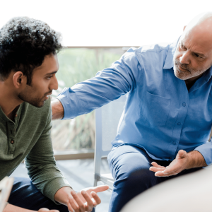 Older man in blue shirt mentoring younger man, demonstrating supportive coaching or counseling interaction