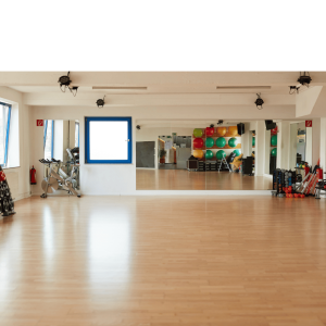 Spacious fitness studio with wooden flooring, wall-mounted mirrors, exercise equipment including stationary bike, colorful stability balls, resistance bands, and training props organized along the walls